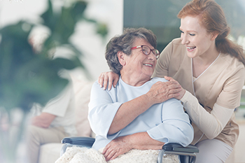 An elderly woman is sitting in a wheelchair and smiling at a nurse